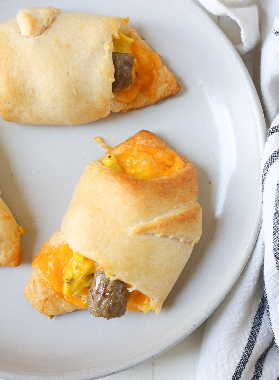 Overhead shot of a crescent roll filled with cheese, scrambled eggs, and a breakfast sausage link