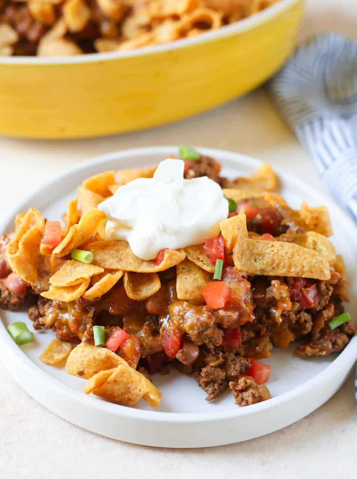Layered casserole with taco seasoned ground beef, tomatoes, beans, and cheese with Fritos on top