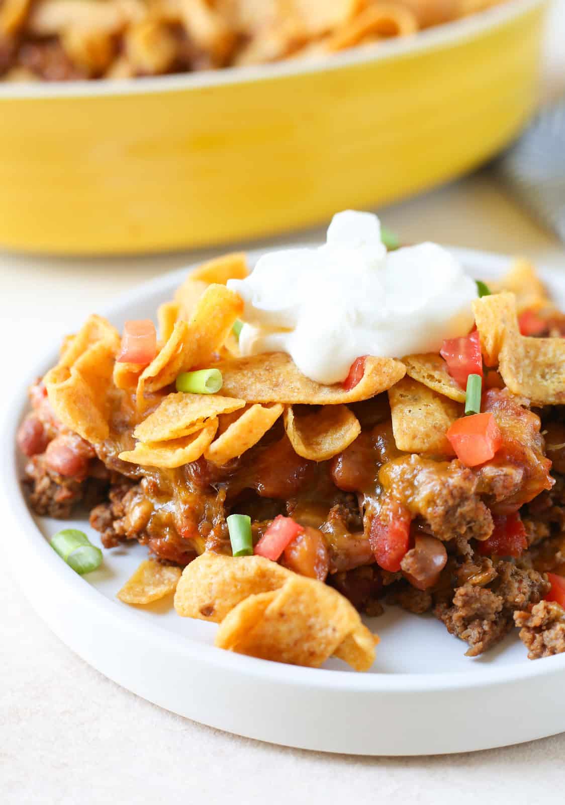 Casserole made with ground beef, tomatoes, cheese, pinto beans, and Fritos. It's topped with sour cream, fresh tomatoes, and green onions. 