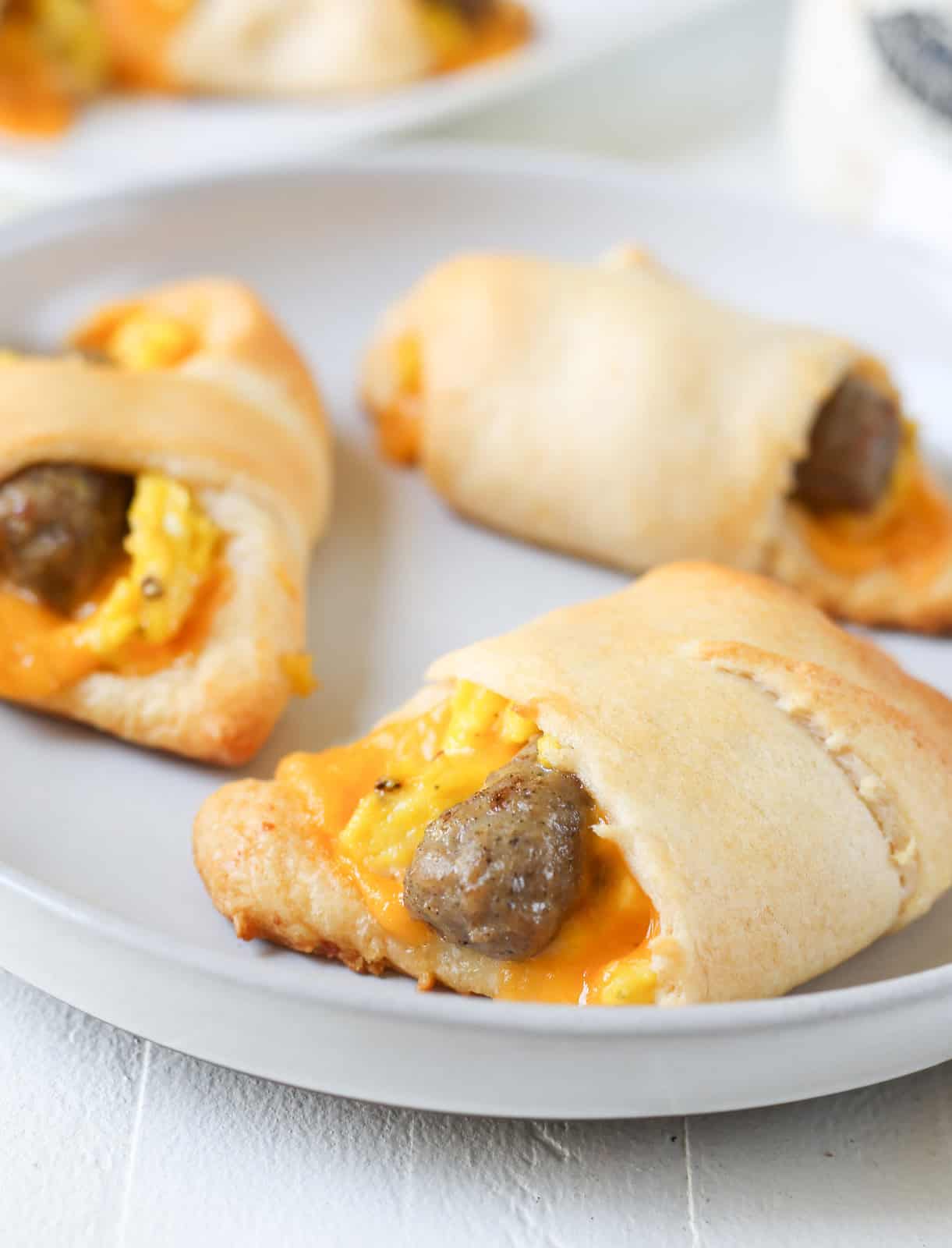 Three crescent rolls filled with cheese, scrambled eggs, and breakfast sausage links