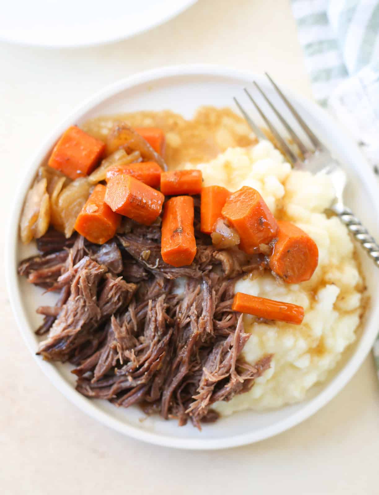 overhead shot of shredded beef, carrots, and onion served over mashed potatoes on a white plate