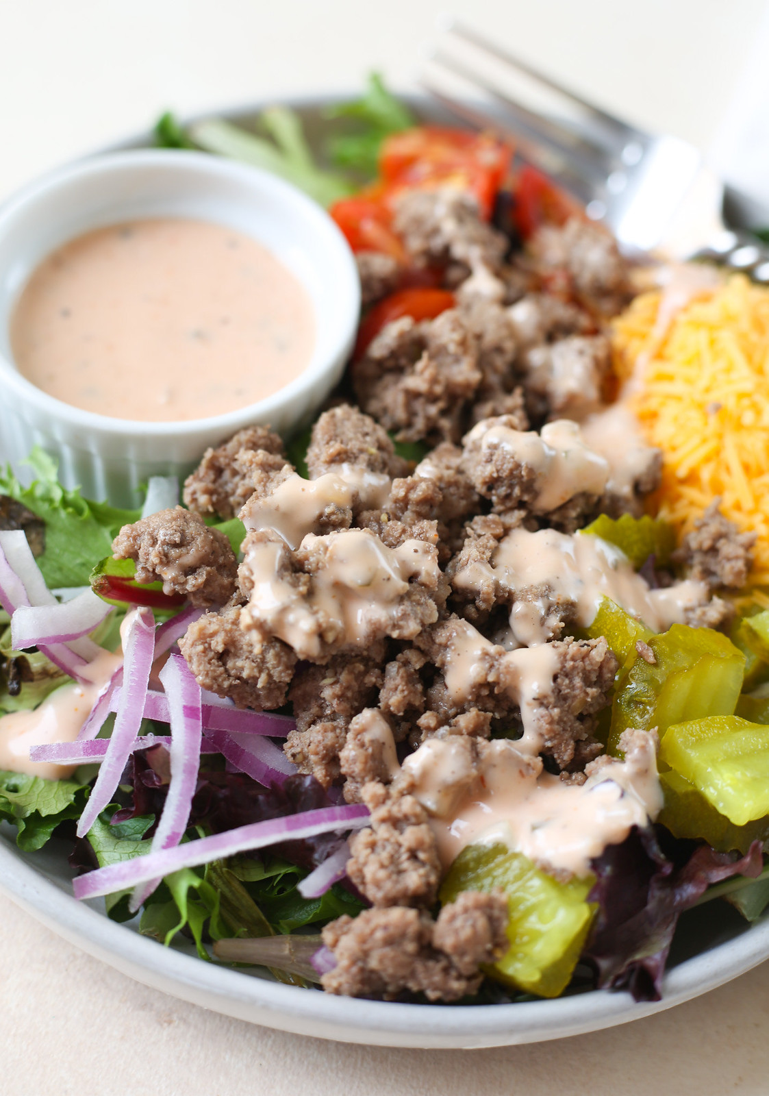 homemade cheesebuger bowls made with lettuce, ground beef, cheddar cheese, red onion, tomatoes, pickles, and a burger sauce on top