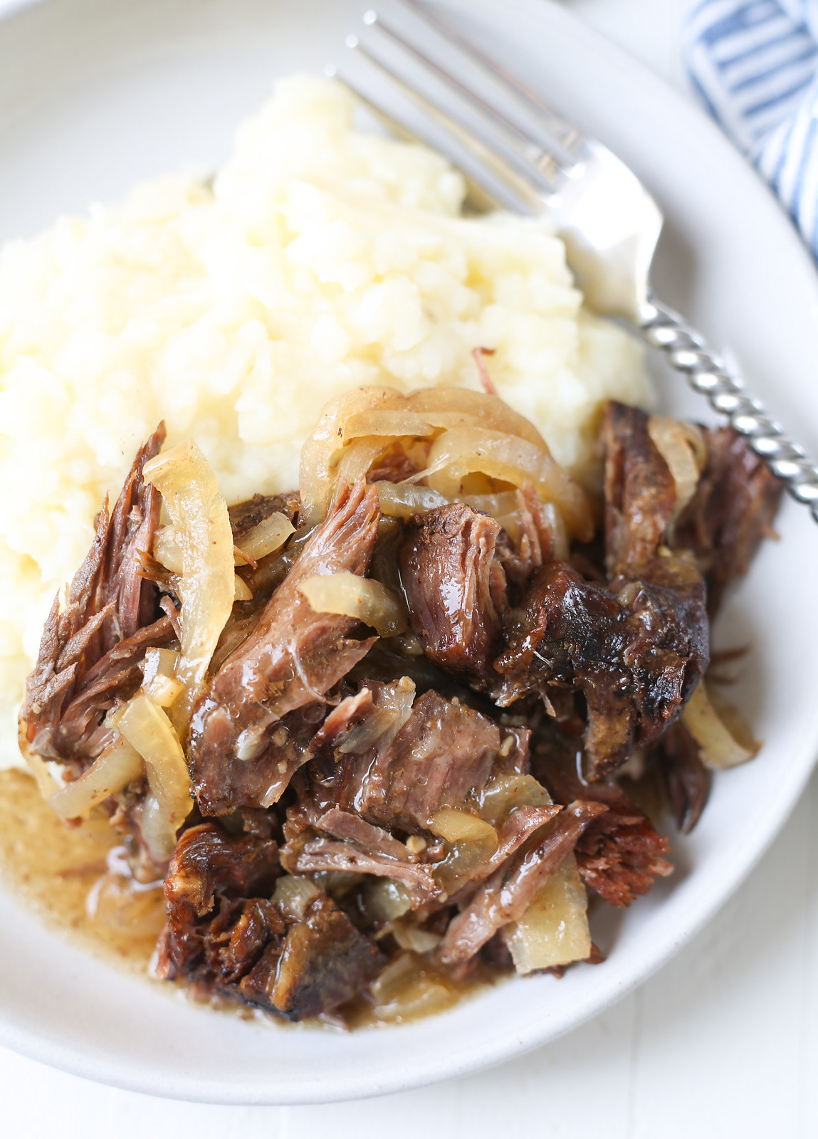 overhead shot of shredded pot roast and onions on top of mashed potatoes
